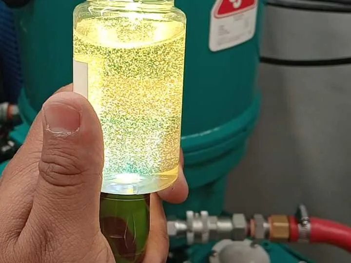Muestra de aceite industrial en frasco tomada junto a la unidad de filtración para su análisis de contaminación.